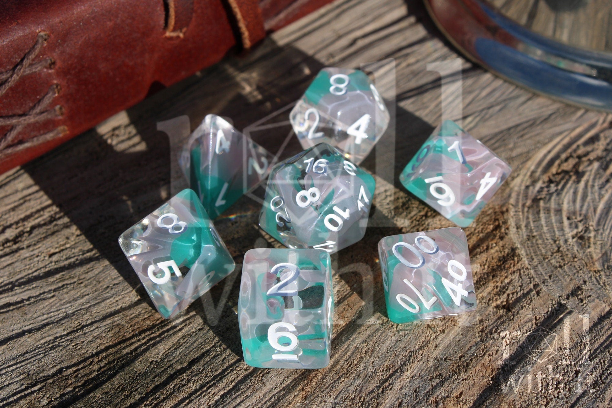 Set of light blue turquoise and white polyhedral roleplaying dice with white numbering on a wooden surface