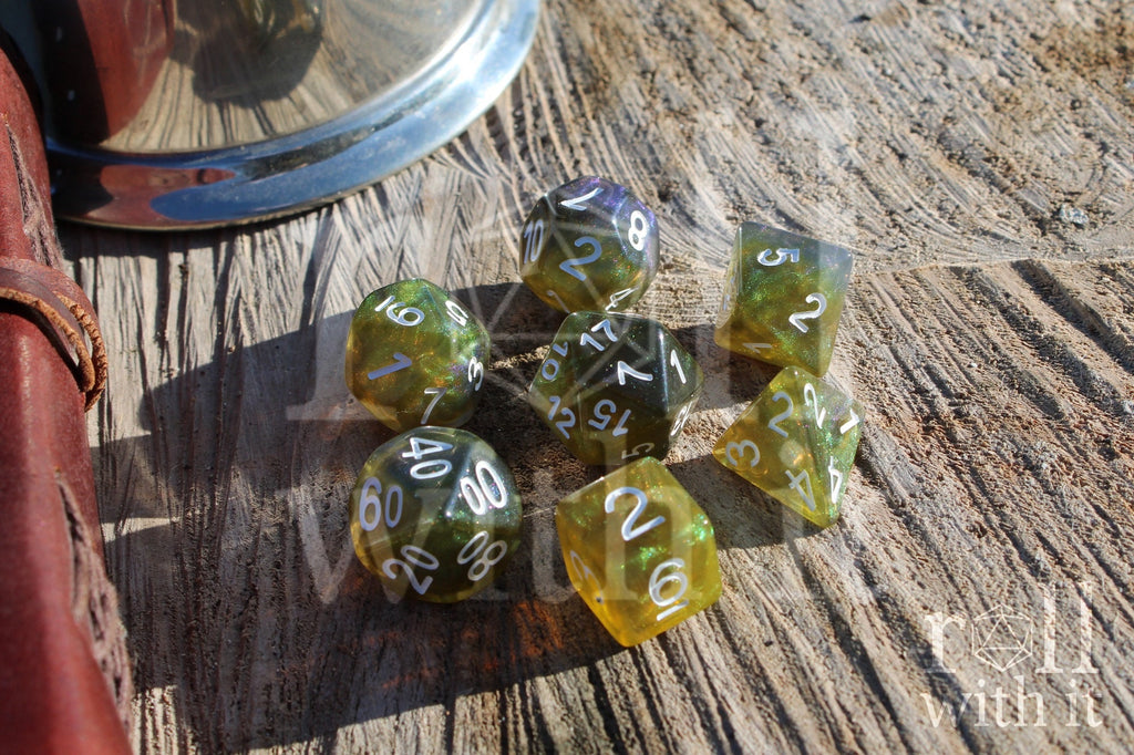 Set of green olive and blue polyhedral dice with white numbers on a wooden surface.
