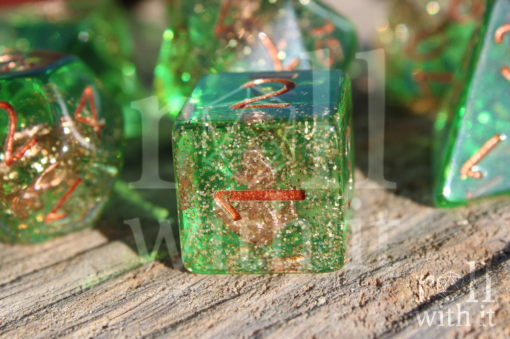 Set of green golden glittery dice with an anchor inside polyhedral dice with copper numbers on a wooden surface