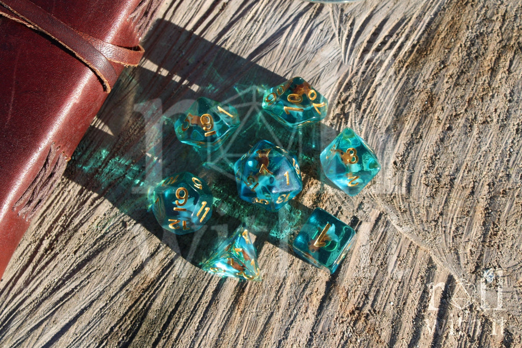 Set of clear blue turquoise polyhedral dice with gold numbers and a mini goldfish inside on a wooden surface