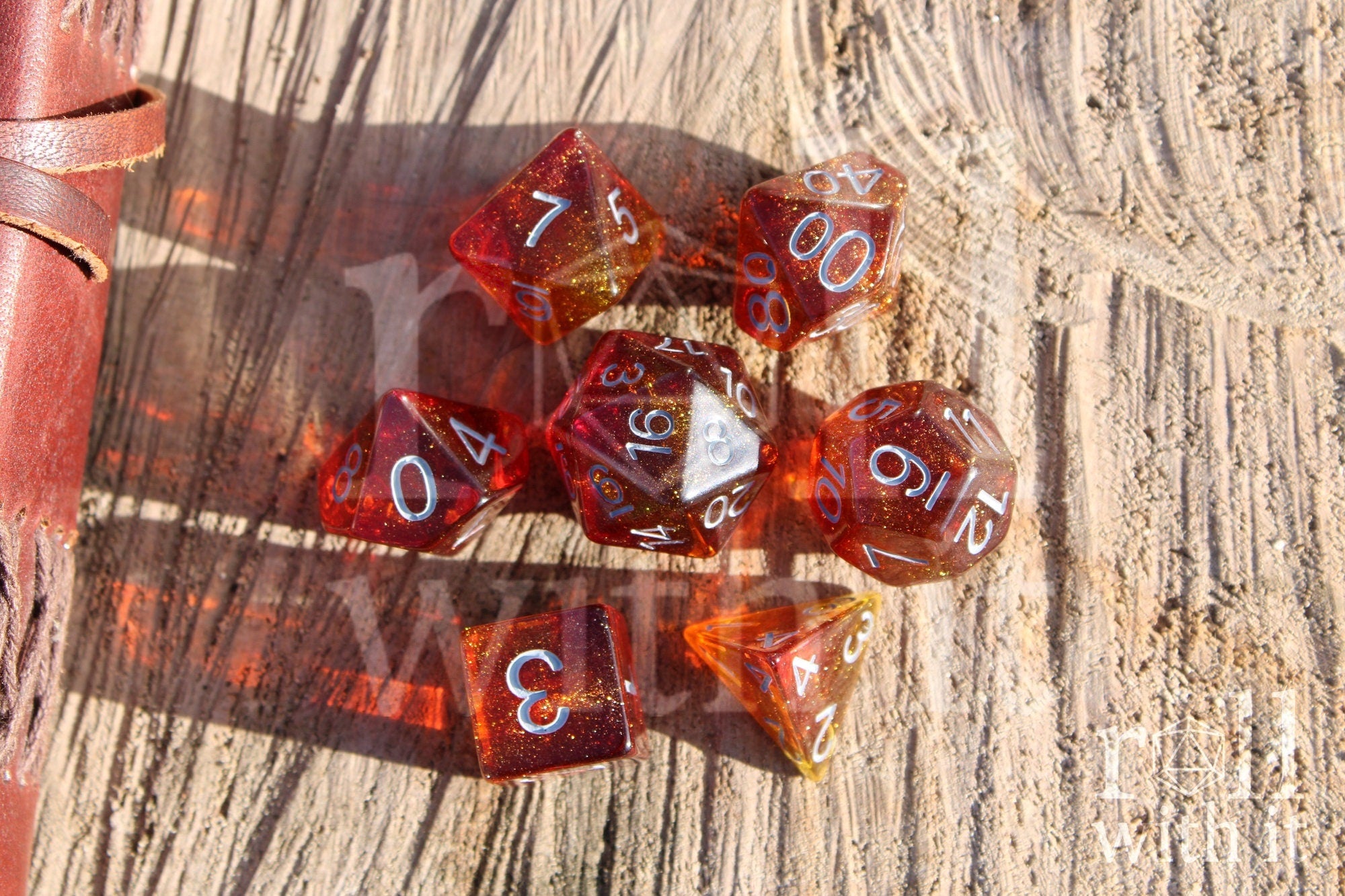 Set of vibrant and glittery red and orange polyhedral TTRPG dice with white numbers on a wooden surface