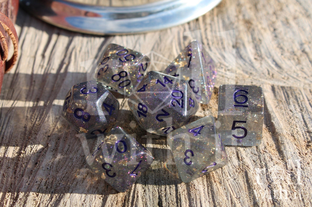 Set of grey shimmering and star like polyhedral dice with gold foil and purple numbers on a wooden background