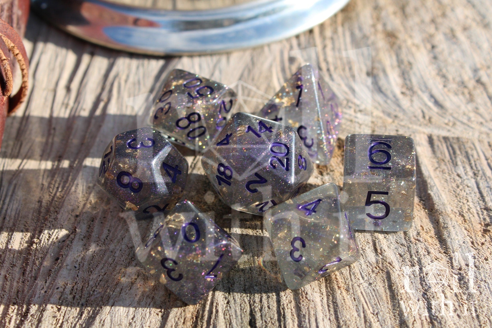 Set of grey shimmering and star like polyhedral dice with gold foil and purple numbers on a wooden background
