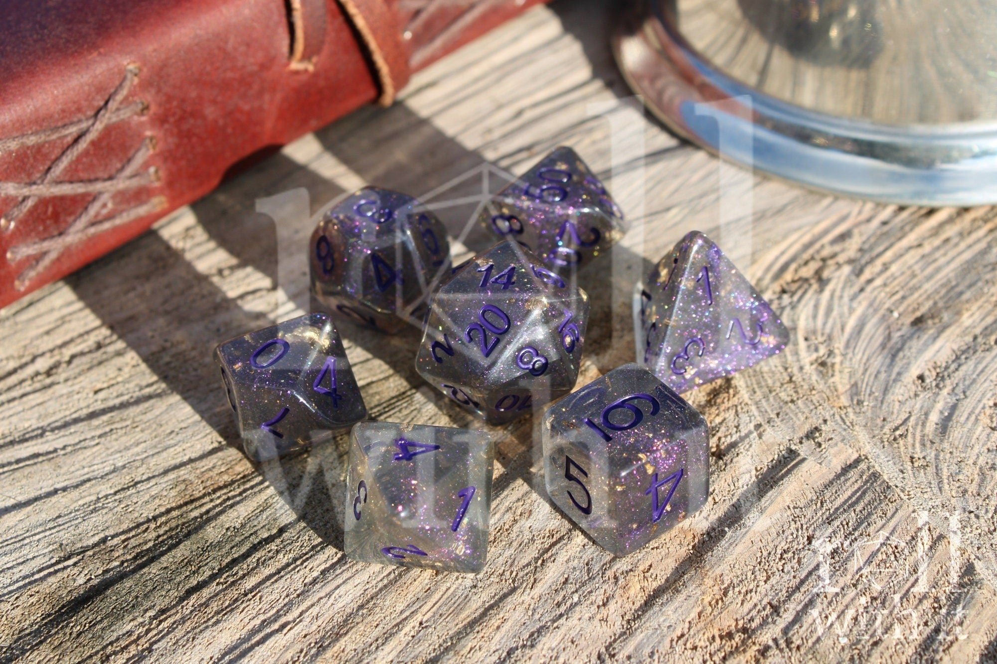 Set of grey shimmering and star like polyhedral dice with gold foil and purple numbers on a wooden background