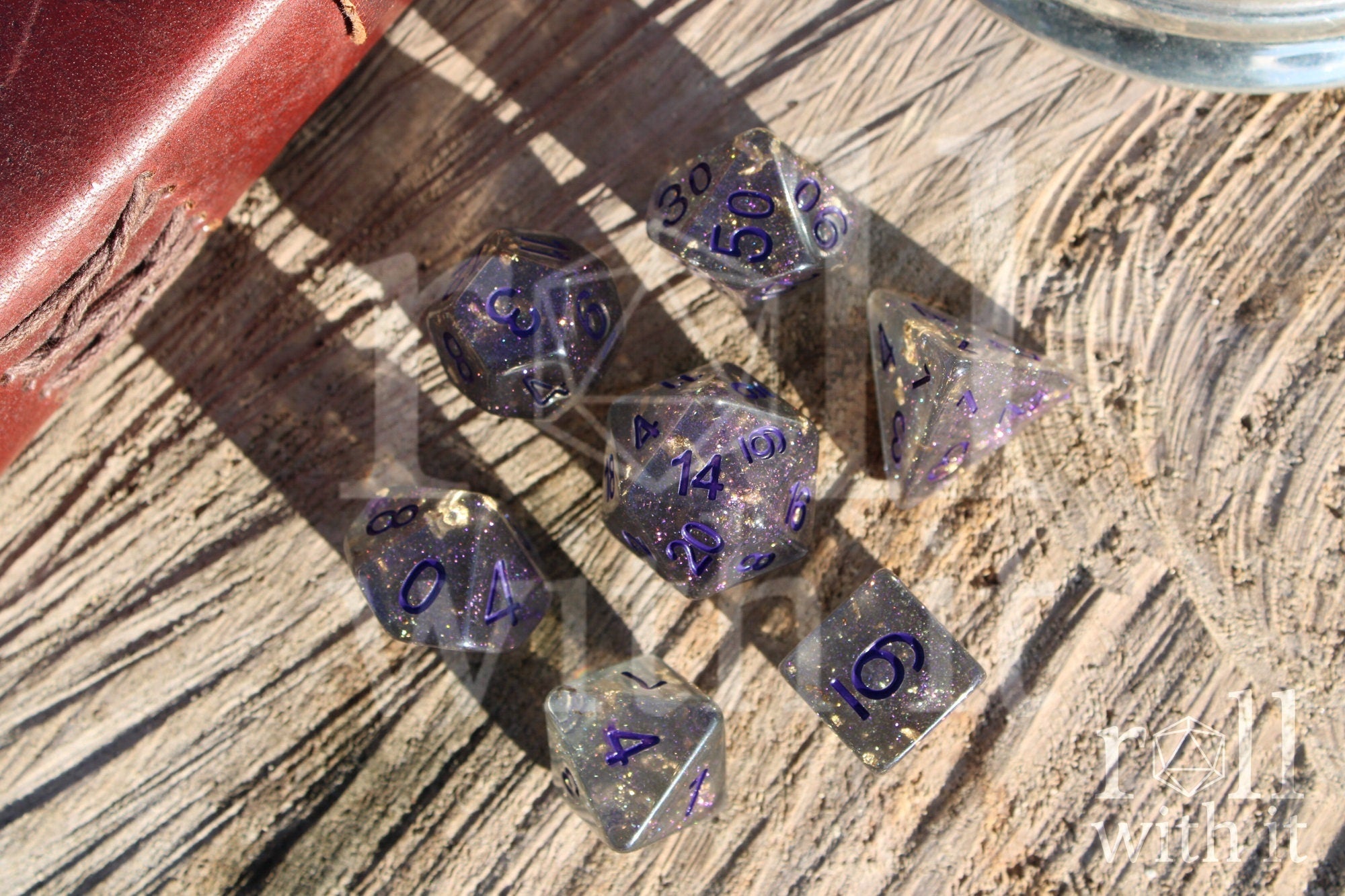 Set of grey shimmering and star like polyhedral dice with gold foil and purple numbers on a wooden background