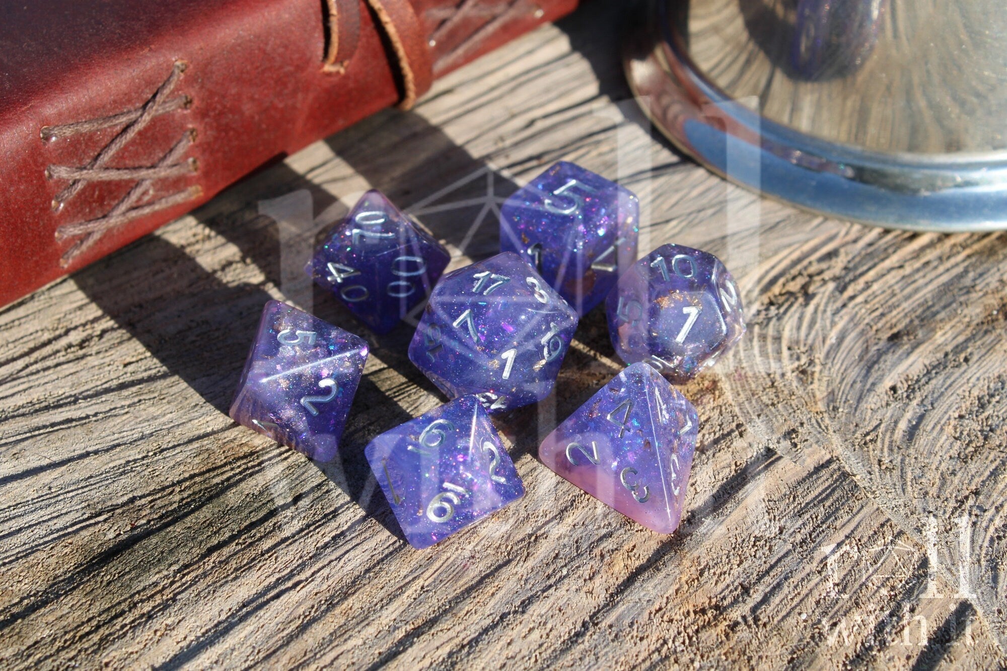 Set of purple, pink glittery and gold leaf polyhedral roleplaying dice with silver lettering on a wooden surface