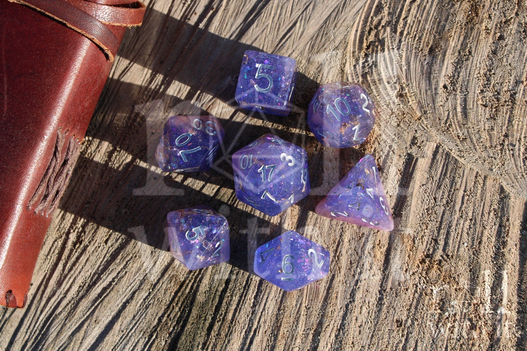 Set of purple, pink glittery and gold leaf polyhedral RGP dice with silver lettering on a wooden surface