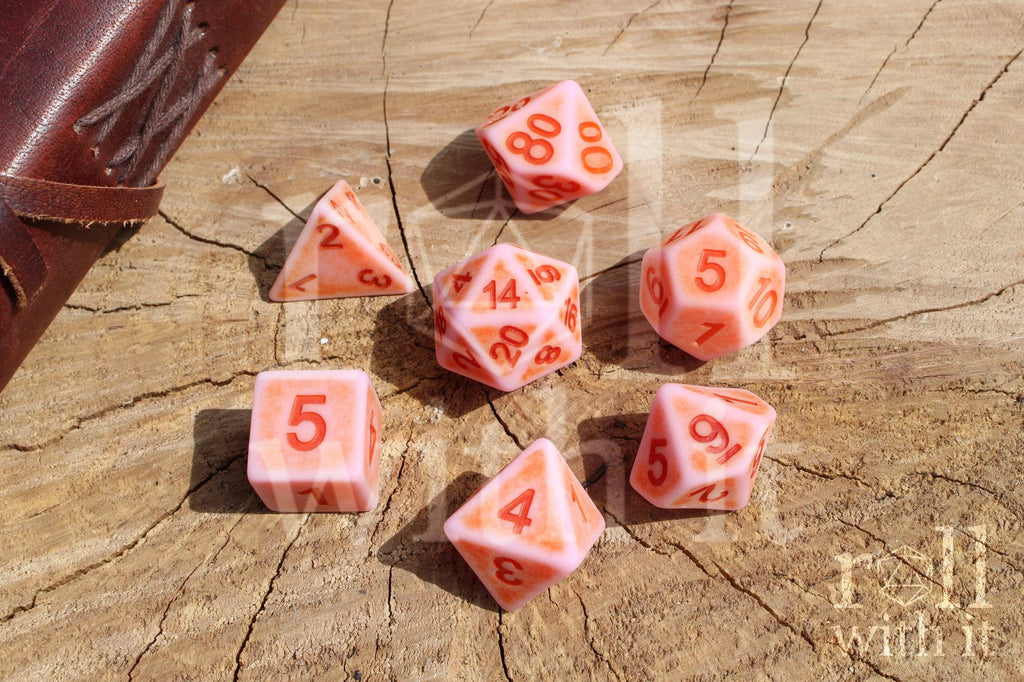 Set of matte pink polyhedral dice with red numbers on a wooden surface