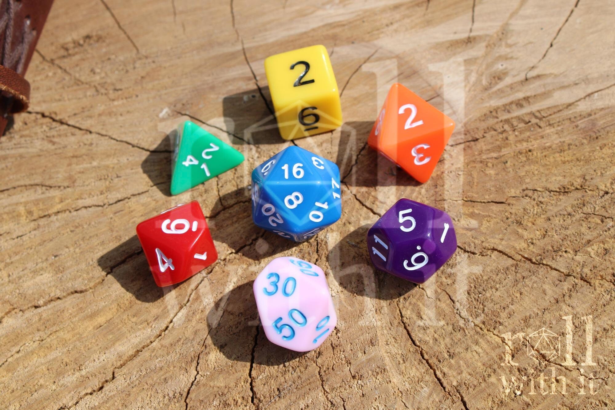 A colourful set of rainbow polyhedral roleplaying dice with white, blue, and black numbers on a wooden surface