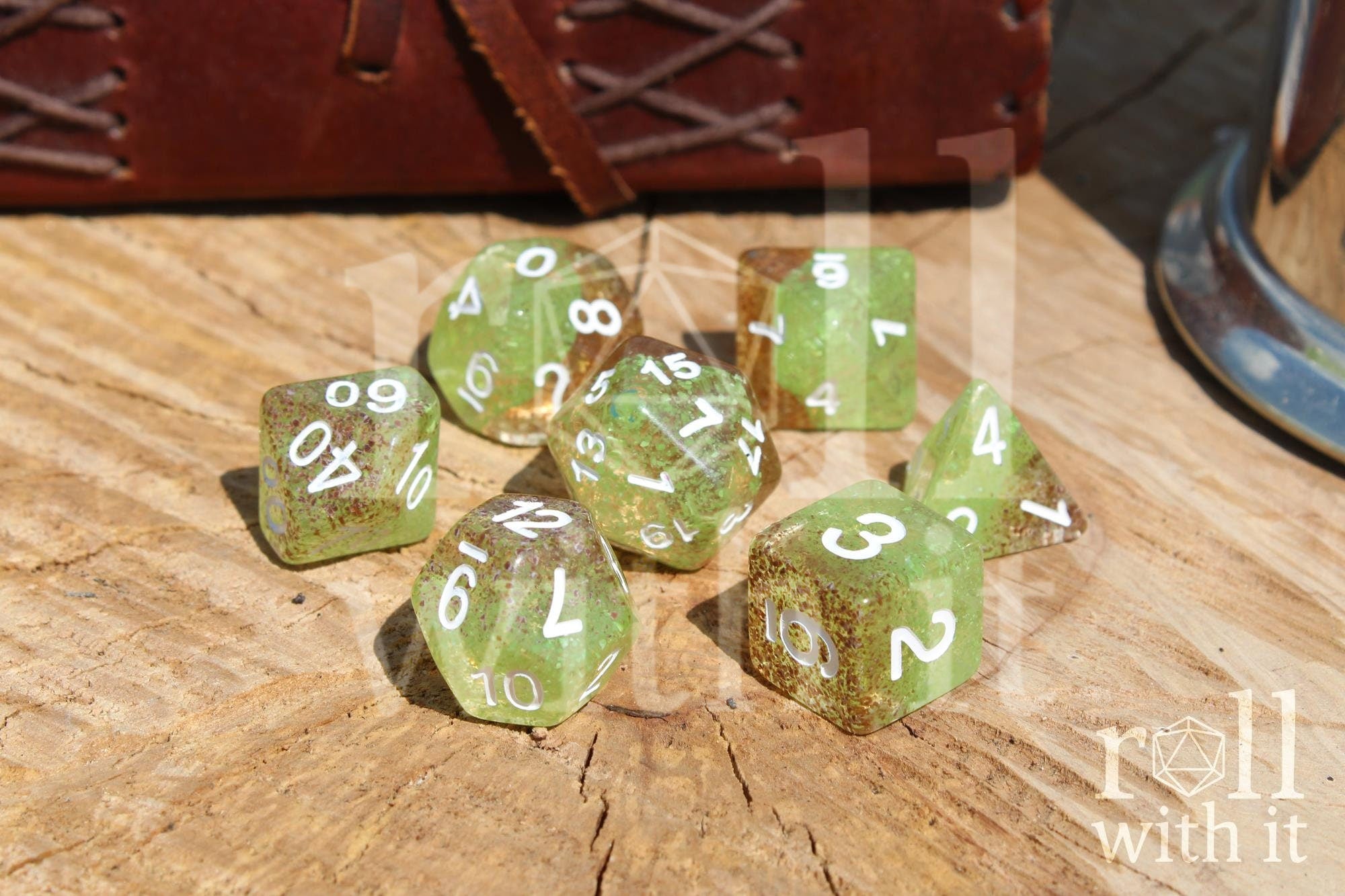 Translucent apple green and ginger brown speckled polyhedral roleplaying dice with white numbers on a wooden surface