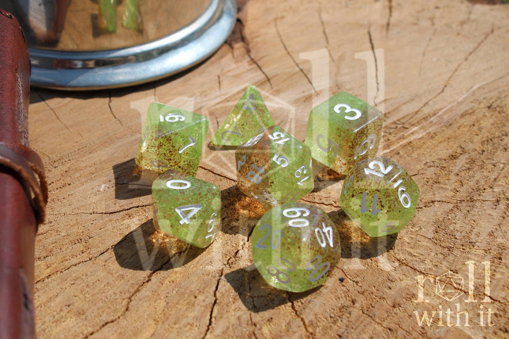 Translucent apple green and ginger brown speckled polyhedral roleplaying dice with white numbers on a wooden surface
