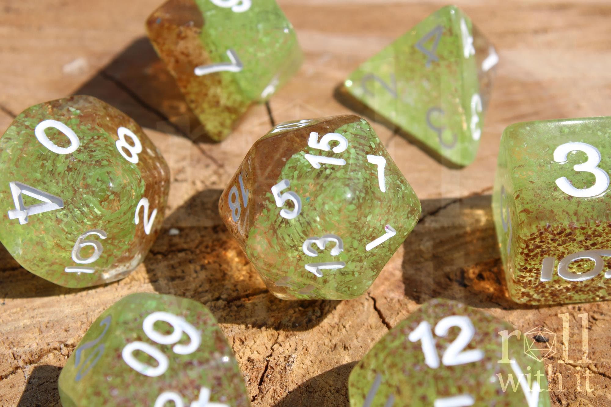 Apple green and ginger brown speckled polyhedral DND dice with white numbers sat on a wooden surface