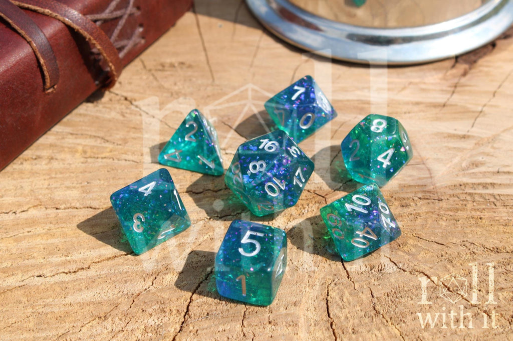 Set of glittery and shining blue and green polyhedral roleplaying dice with silver leaf inside on a wooden surface