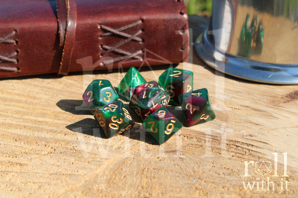 Set of glittery and shimmering green and purple polyhedral dice with gold numbers on a wooden surface