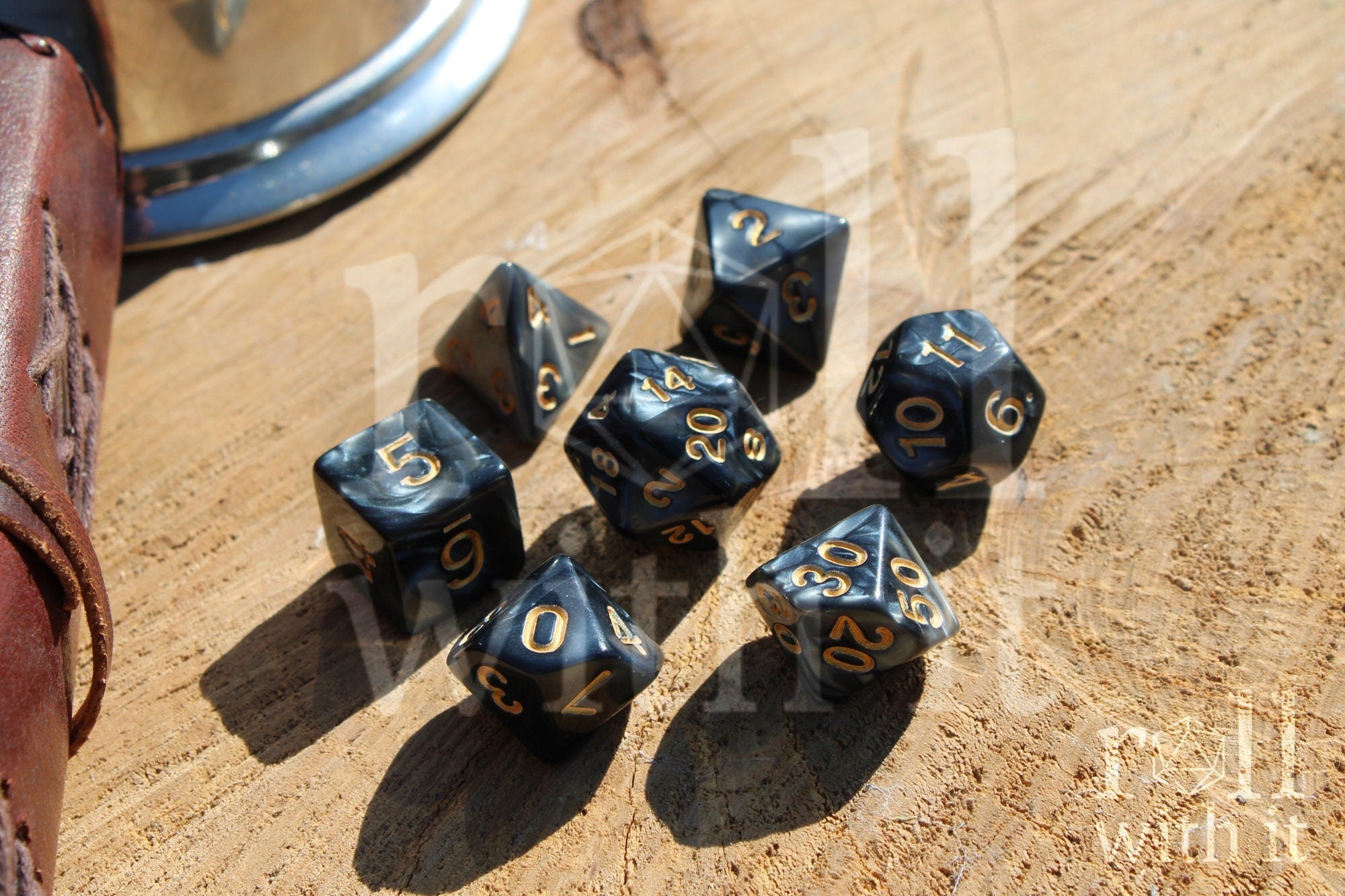 Set of black swirling polyhedral dice with gold numbers on a wooden surface