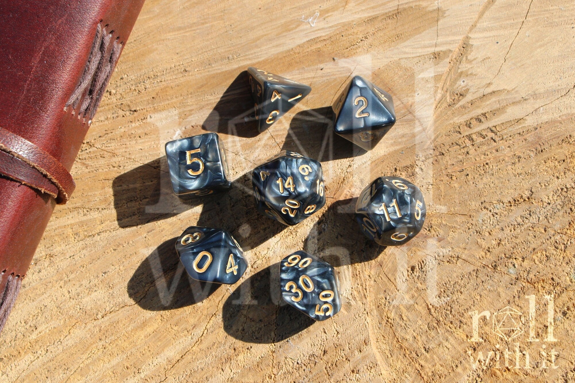 Set of black swirling polyhedral DnD dice with gold numbers on a wooden surface