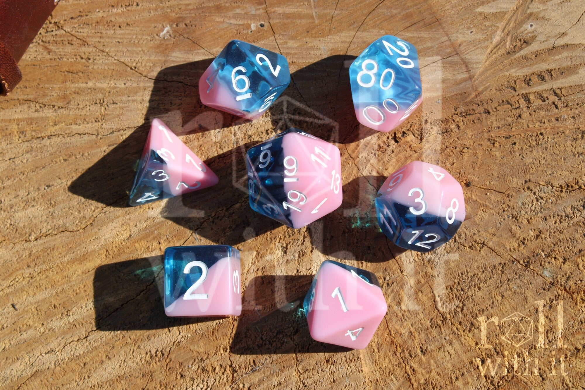 Set of bubblegum pink and clear blue polyhedral roleplaying dice on a wooden surface