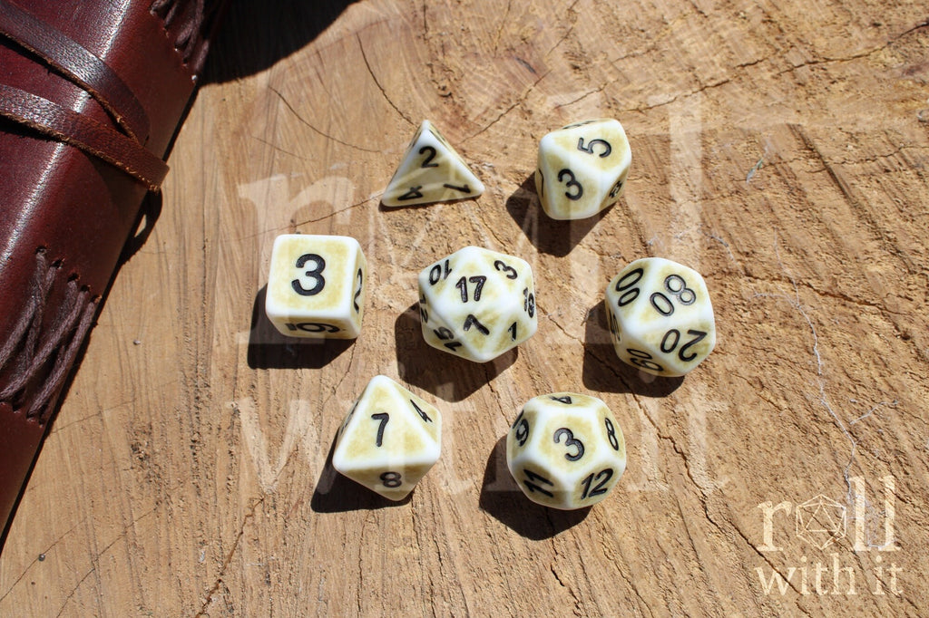 Set of rustic looking creamy bone white matte DnD dice with black numbers on a wooden surface