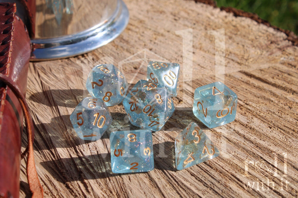 Set of clear blue and gold foil dice with gold numbers on a wooden surface