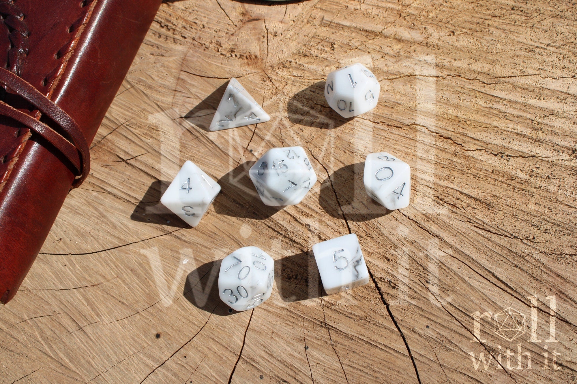 Granite white polyhedral DND dice with silver numbering on a wooden surface.