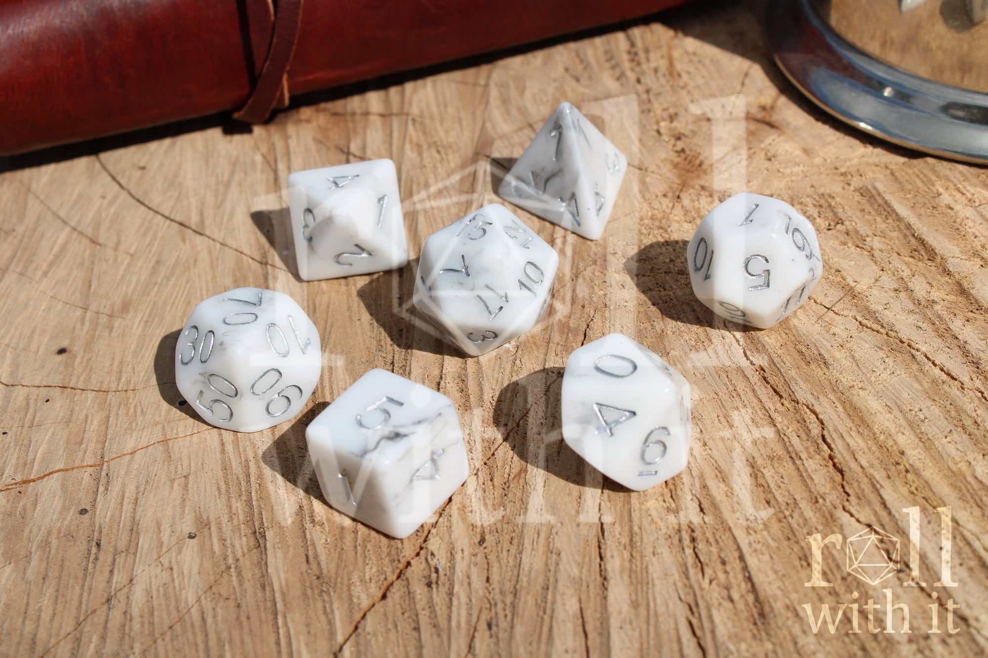 Granite white polyhedral DND dice with silver numbering on a wooden surface.