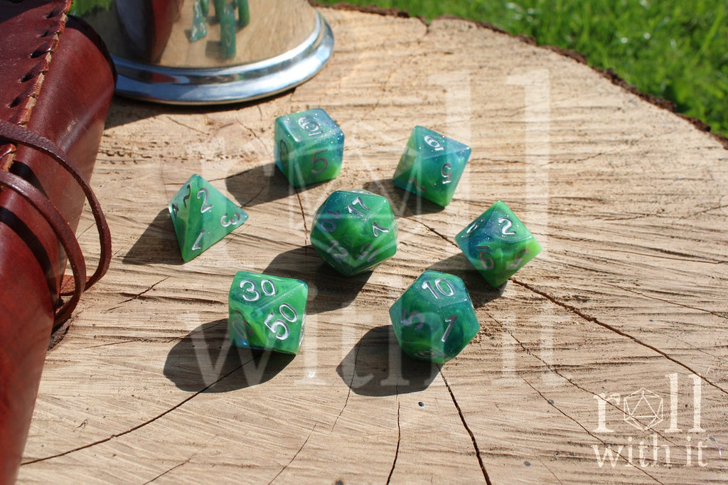 Set of green and blue glittery polyhedral dice with silver numbers on a wooden surface