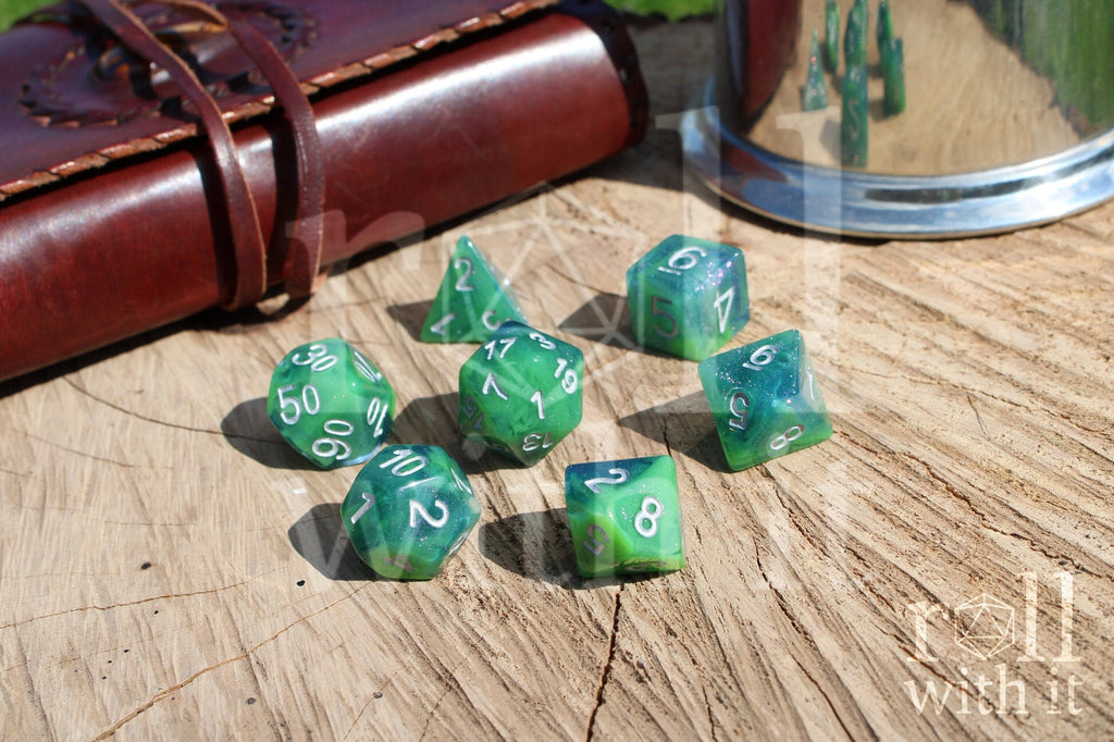 Set of green and blue glittery polyhedral dice with silver numbers on a wooden surface