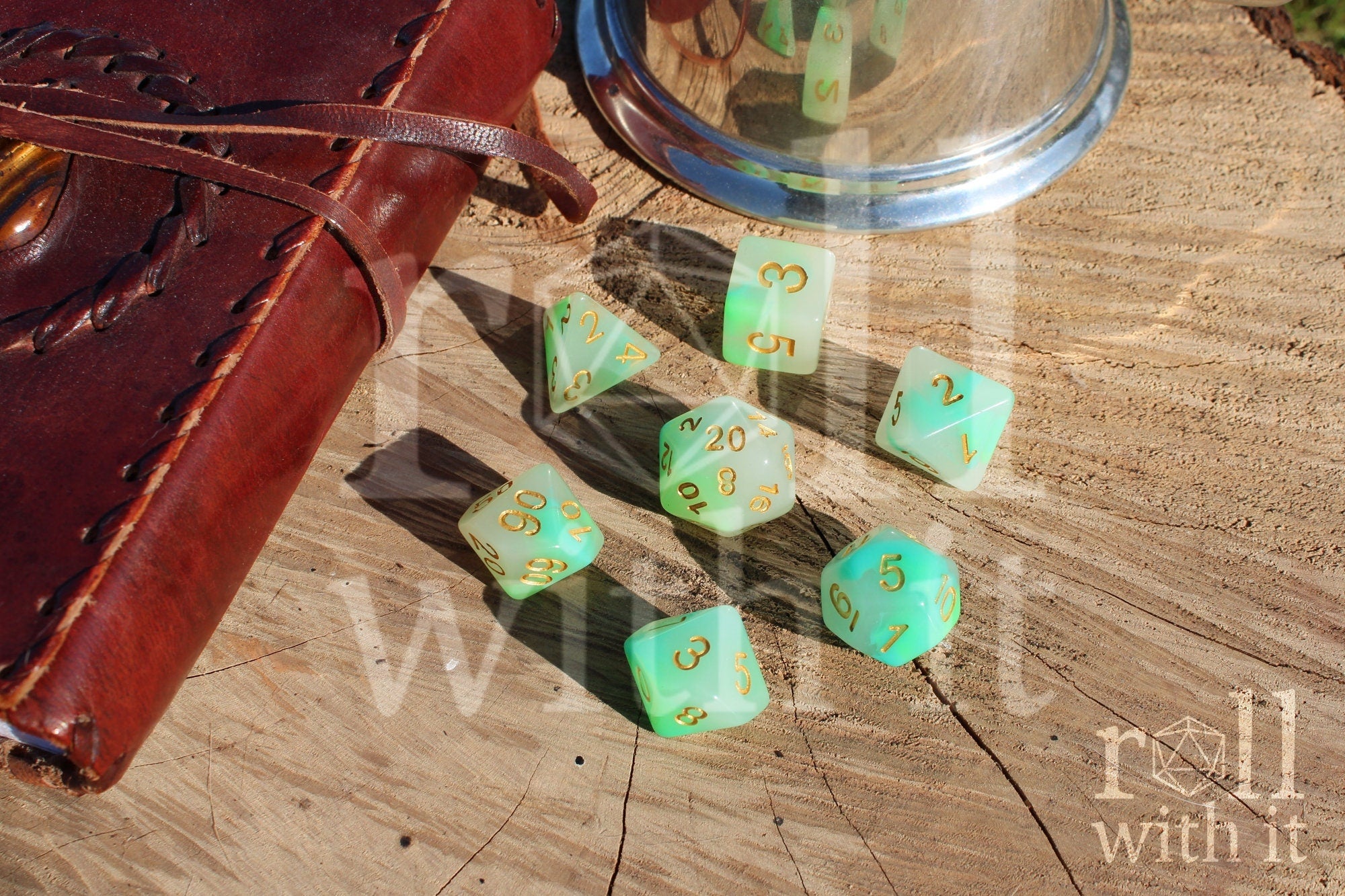 Set of turquoise and green polyhedral DND dice with gold numbers on a wooden surface with roleplaying game accessories in the background