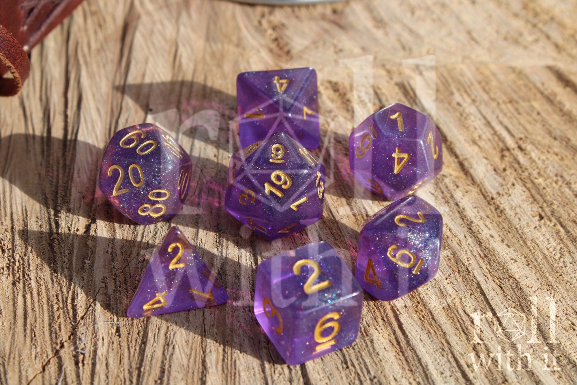 Set of glittery purple polyhedral dice with gold numbers on a wooden surface