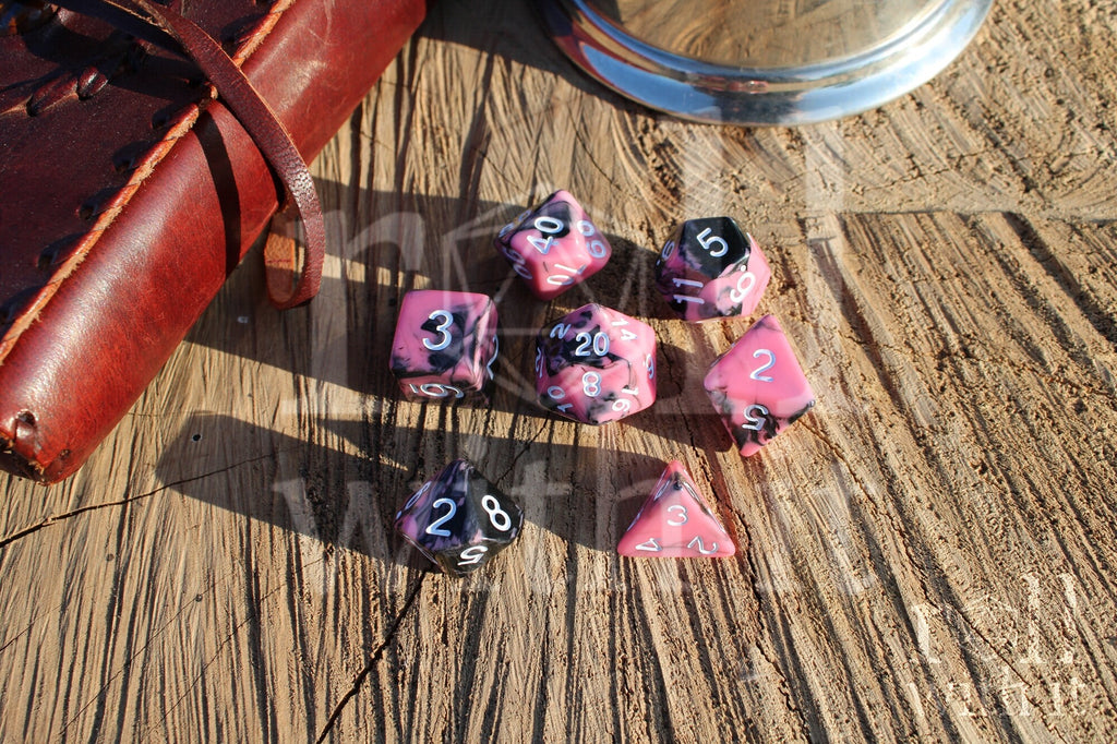 Set of pink and black swirling polyhedral roleplaying dice with white numbers on a wooden surface