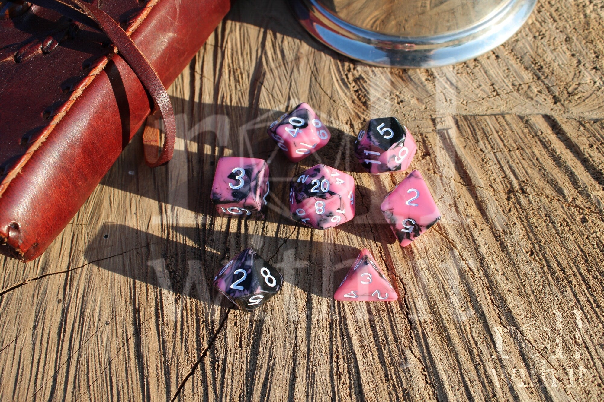Set of pink and black swirling polyhedral roleplaying dice with white numbers on a wooden surface