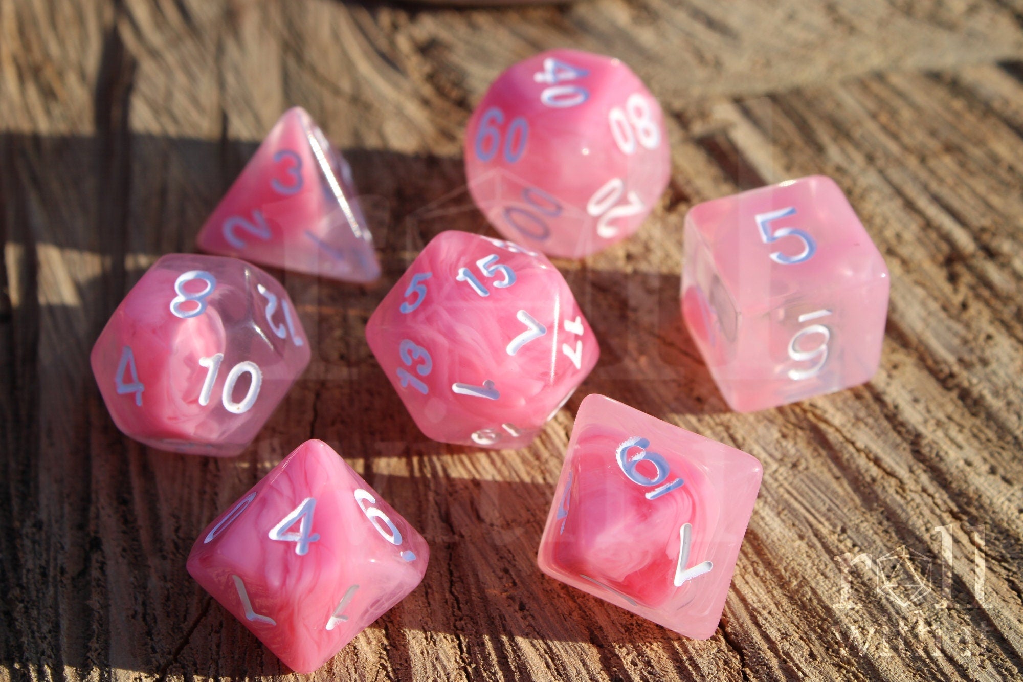 Set of cloudy pink and clear polyhedral roleplaying dice with white numbers on a wooden surface