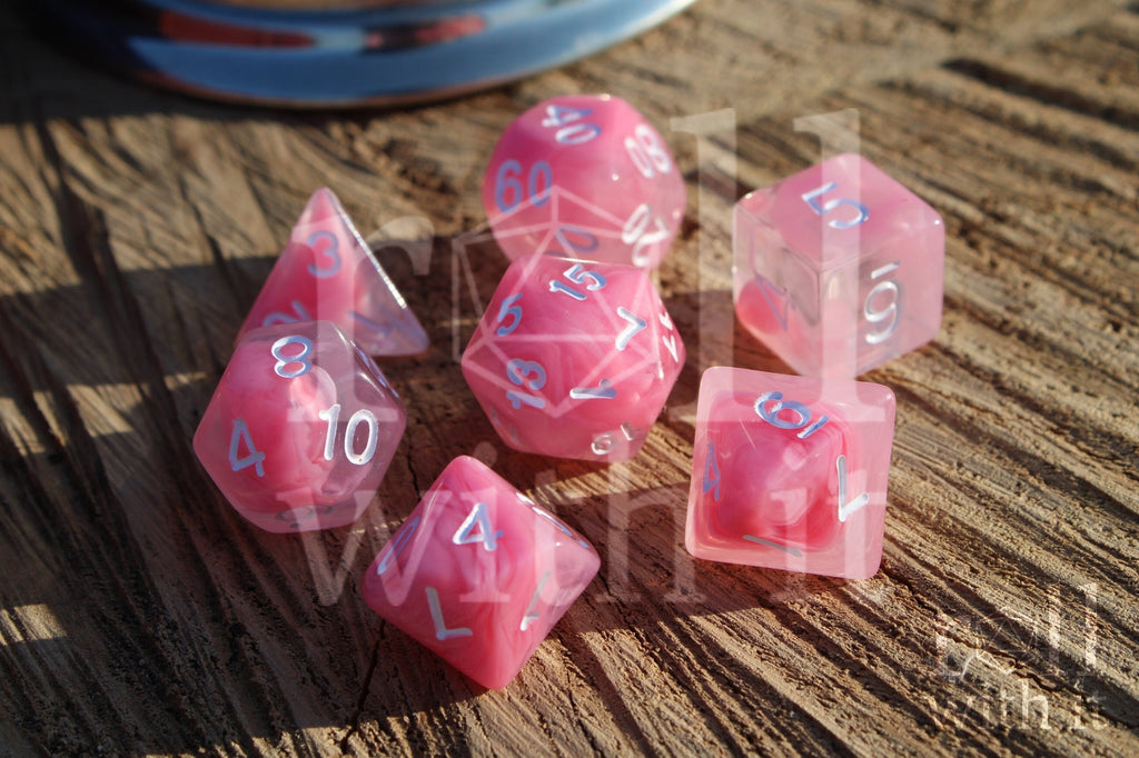 Set of cloudy pink and clear polyhedral DND dice with white numbers on a wooden surface