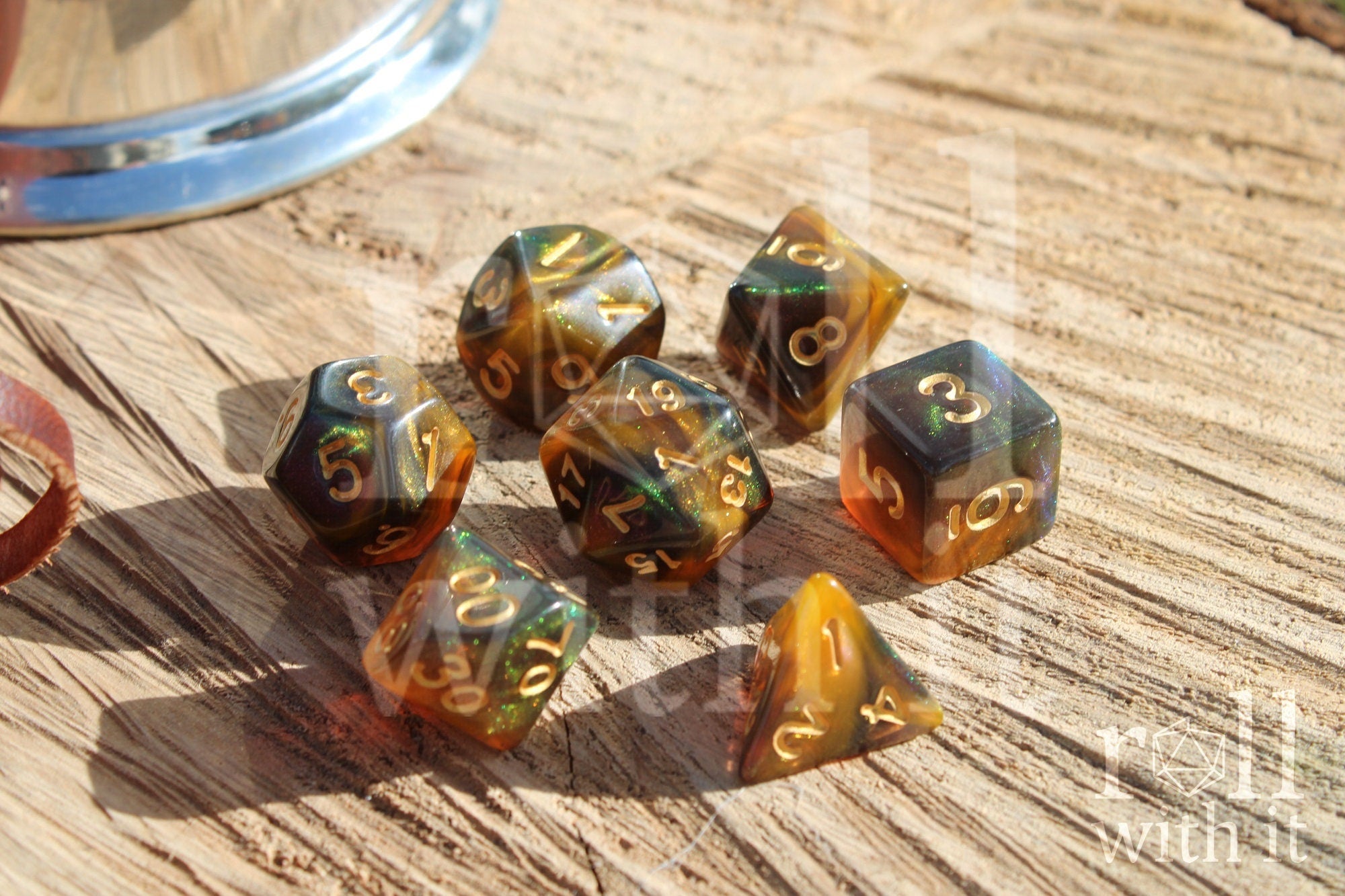 Set of 7 glittery green, smoky amber and orange swirling polyhedral roleplaying dice on a wooden surface.