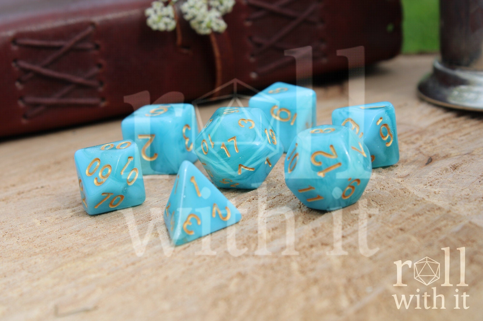 Set of aqua blue polyhedral dice with gold numbers on a wooden surface.