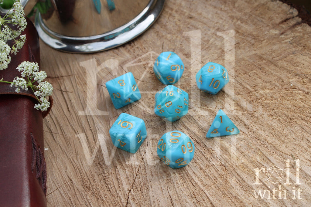 Set of aqua blue polyhedral roleplaying dice with gold numbers on a wooden surface.