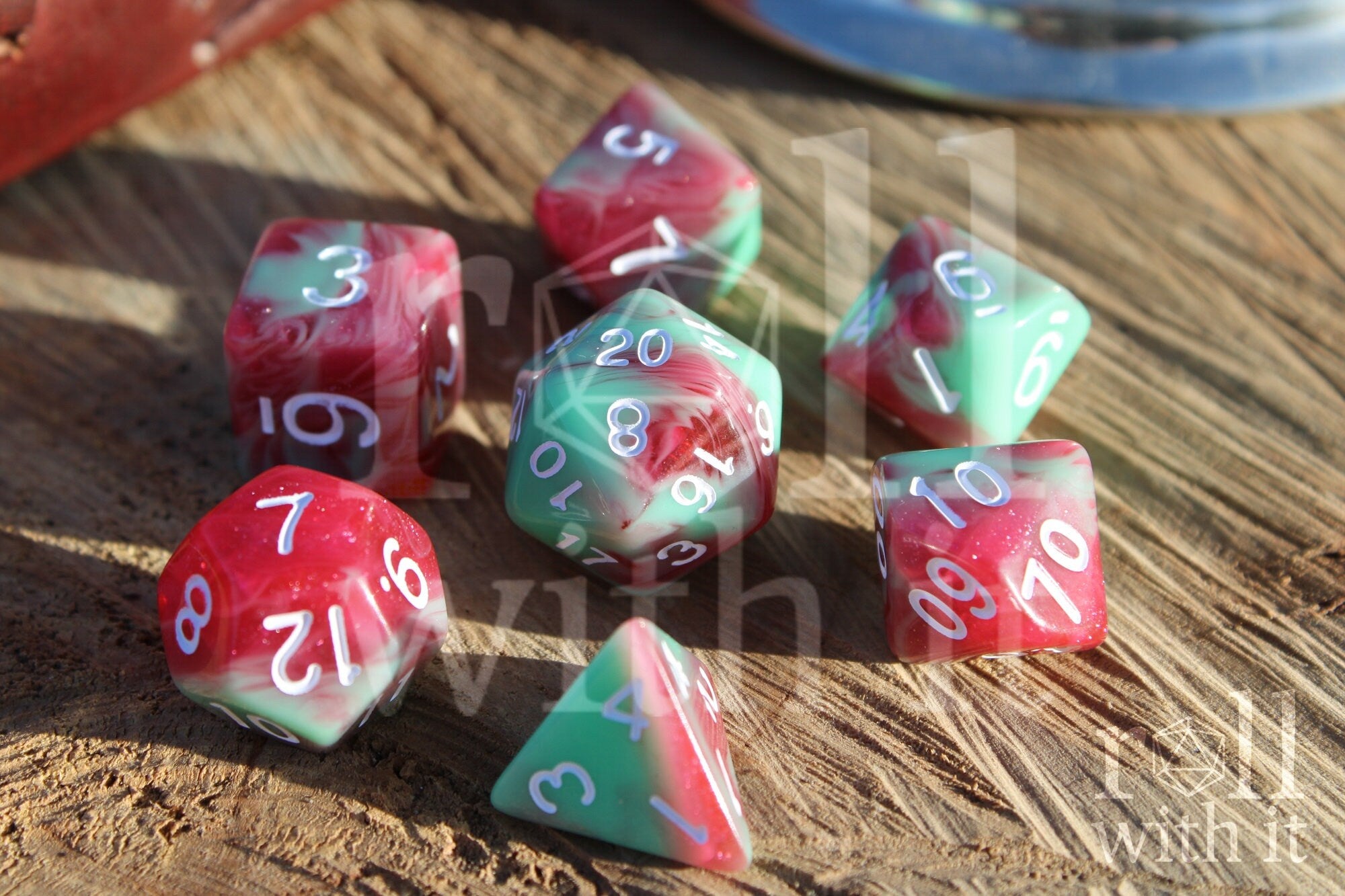Set of glittery red and pastel green polyhedral DnD roleplaying dice on a wooden surface