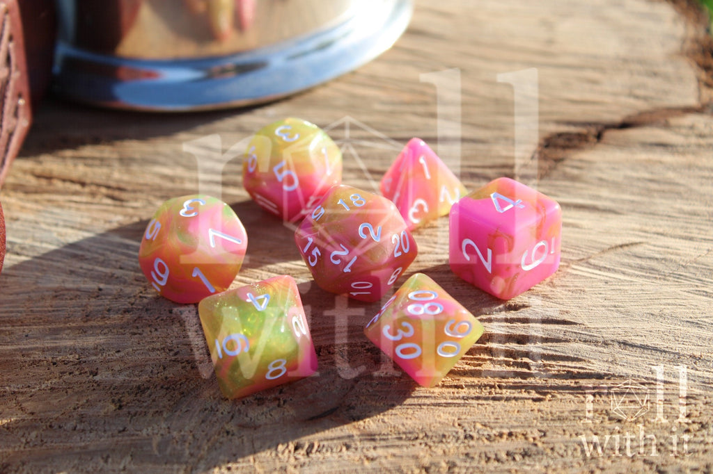Set of candy pink and green with glitter TTRPG polyhedral dice on a wooden surface