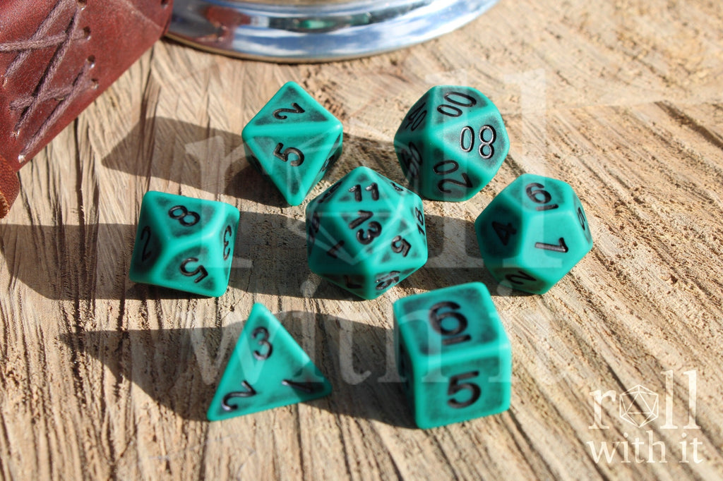 Matte teal polyhedral dice set with black letters on a wooden surface