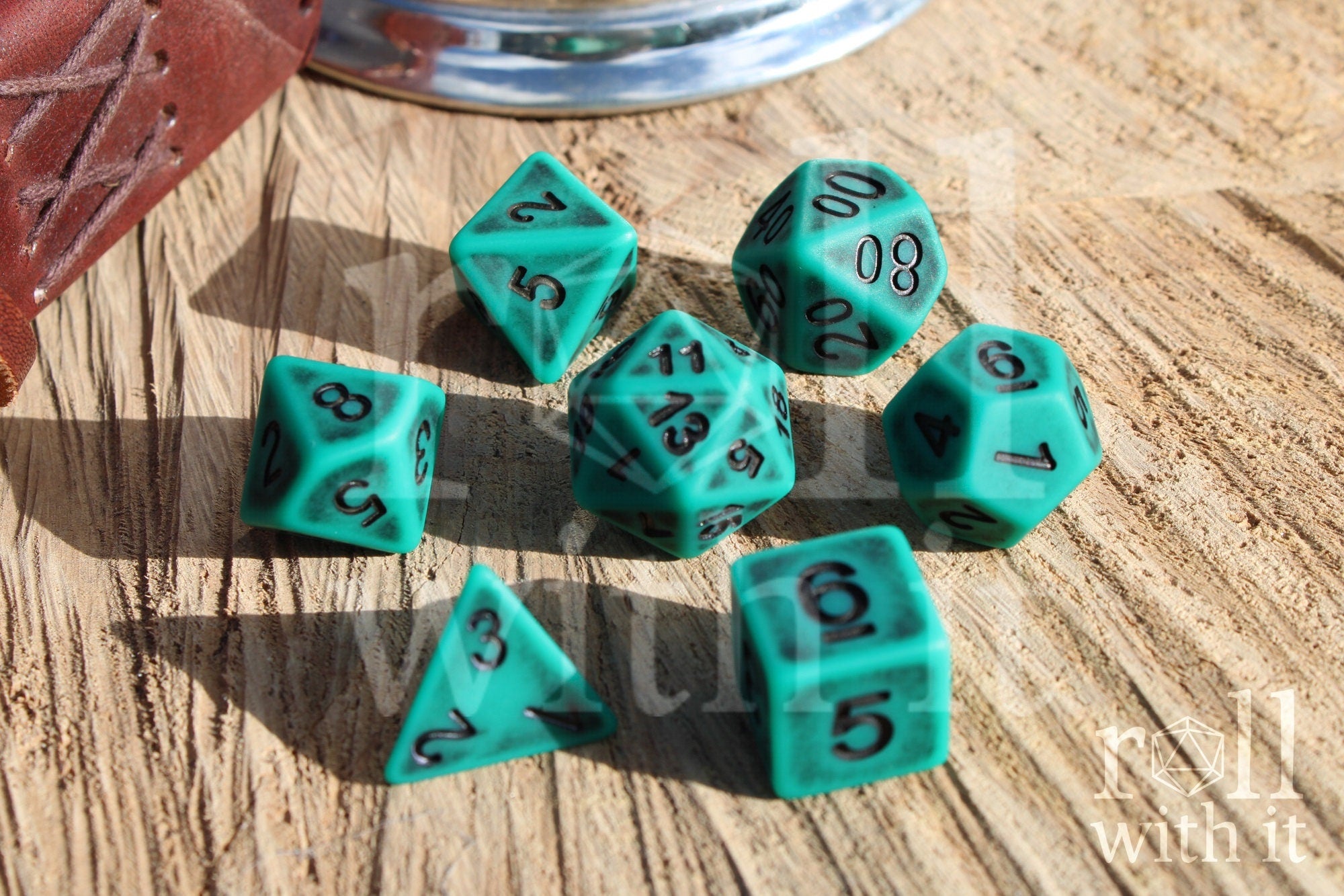 Matte teal polyhedral dice set with black letters on a wooden surface