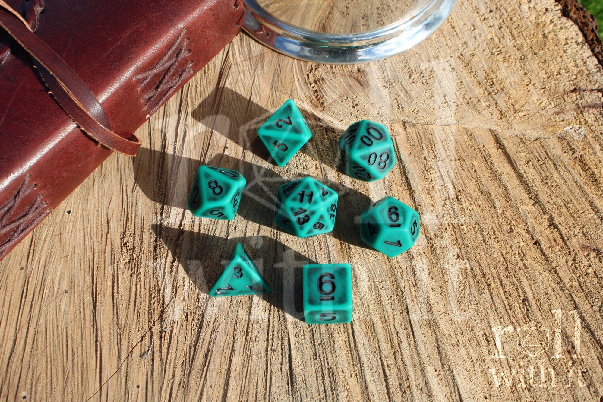 Matte teal polyhedral dice set with black letters on a wooden surface
