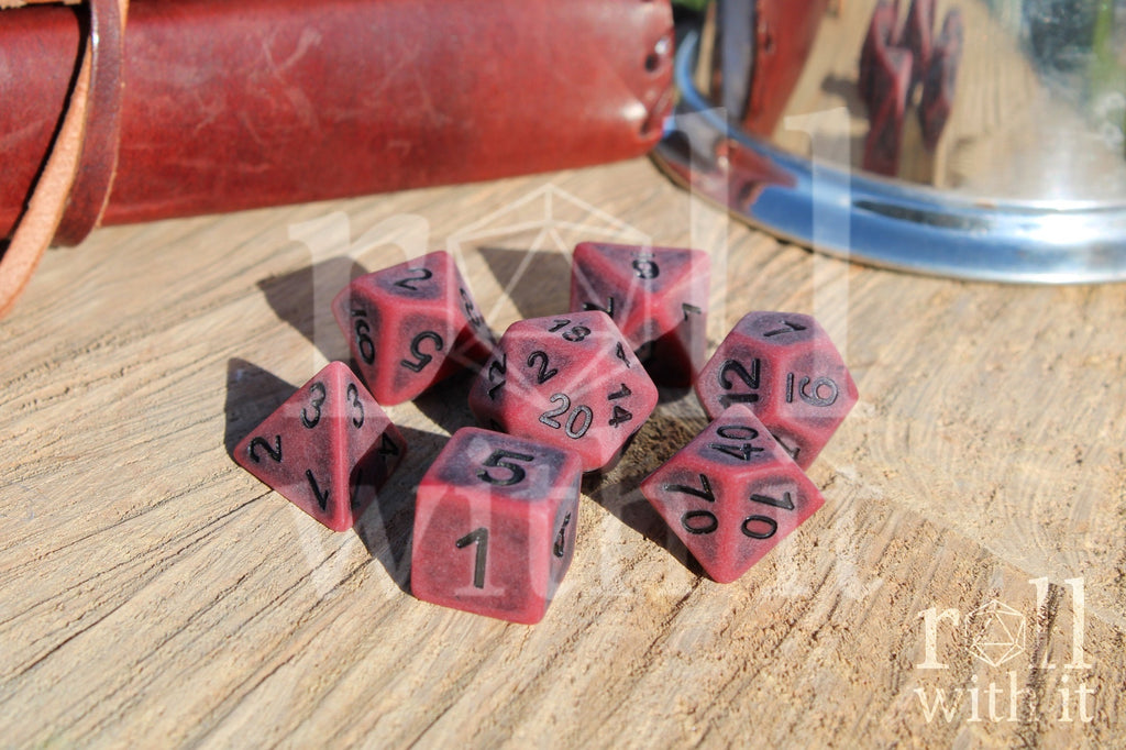 Matte red polyhedral roleplaying dice with a worn look with black lettering set on a wooden surface
