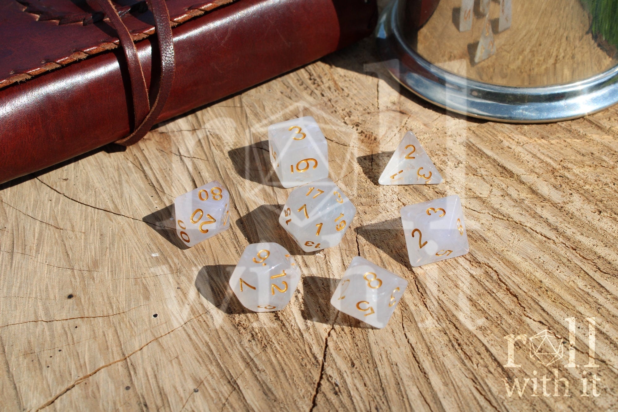A set of silvery grey polyhedral RGP dice with gold numbers on a wooden 