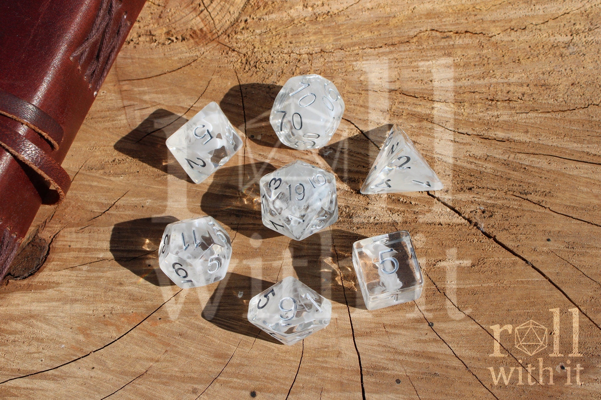 A set of 7 clear and white smoky polyhedral roleplaying dice with silver numbers on a wooden surface