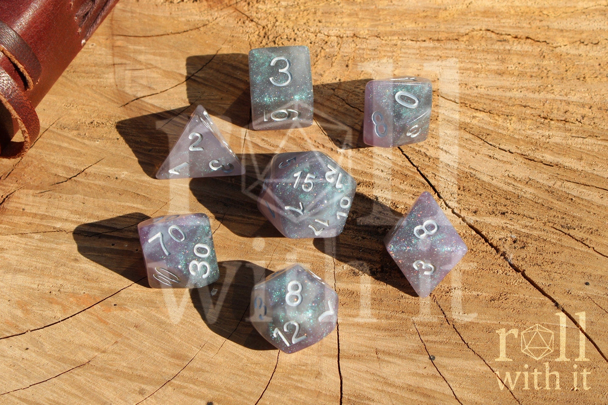 Set of silver and violet glittery polyhedral roleplaying dice with numbers on a wooden surface