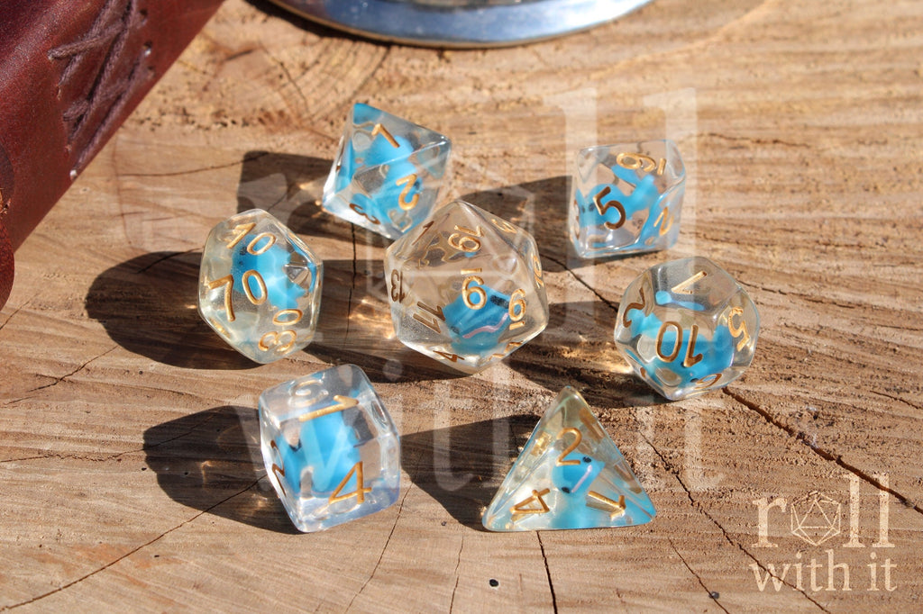 Set of clear polyhedral role playing dice with a small blue whale inside, with gold numbering on a wooden surface