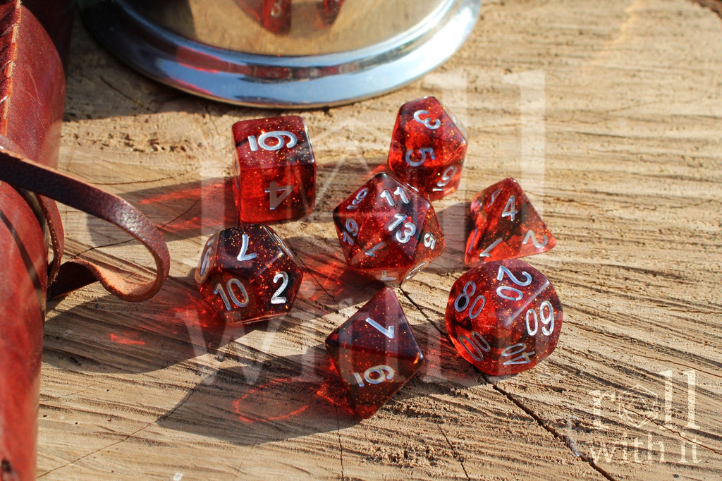 Set of red and black glittery polyhedral DnD dice with silver numbers on a wooden surface