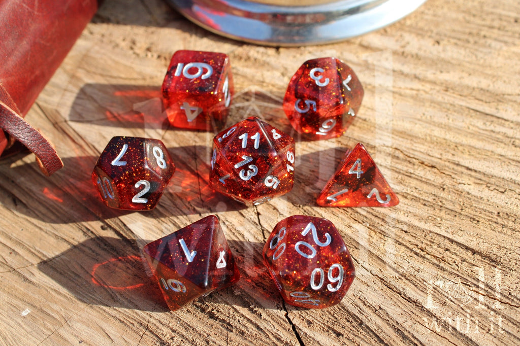 Set of red and black glittery polyhedral roleplaying dice with silver numbers on a wooden surface