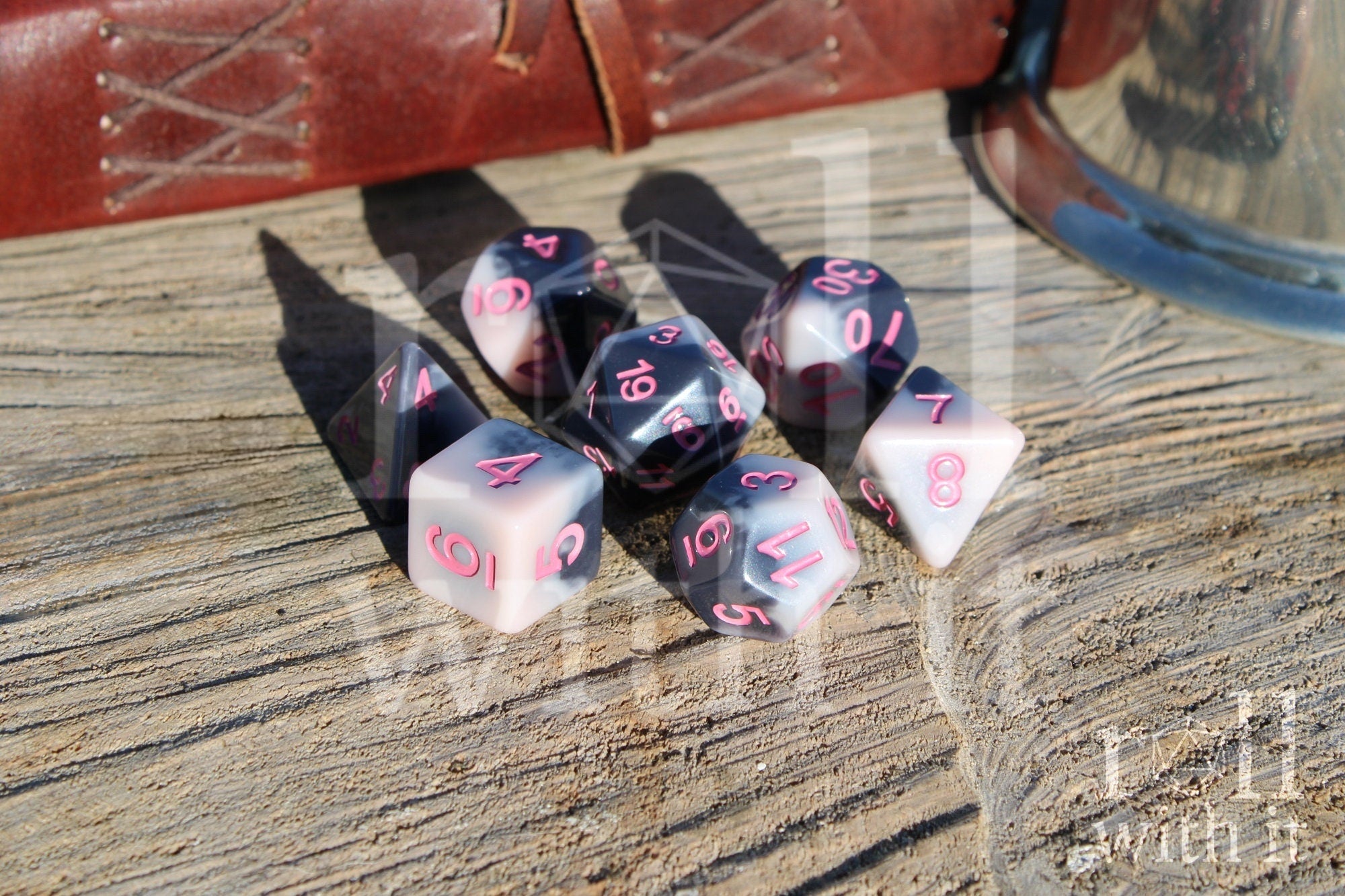Set of pastel pink and grey polyhedral roleplaying dice with pink numbers sat on a wooden surface
