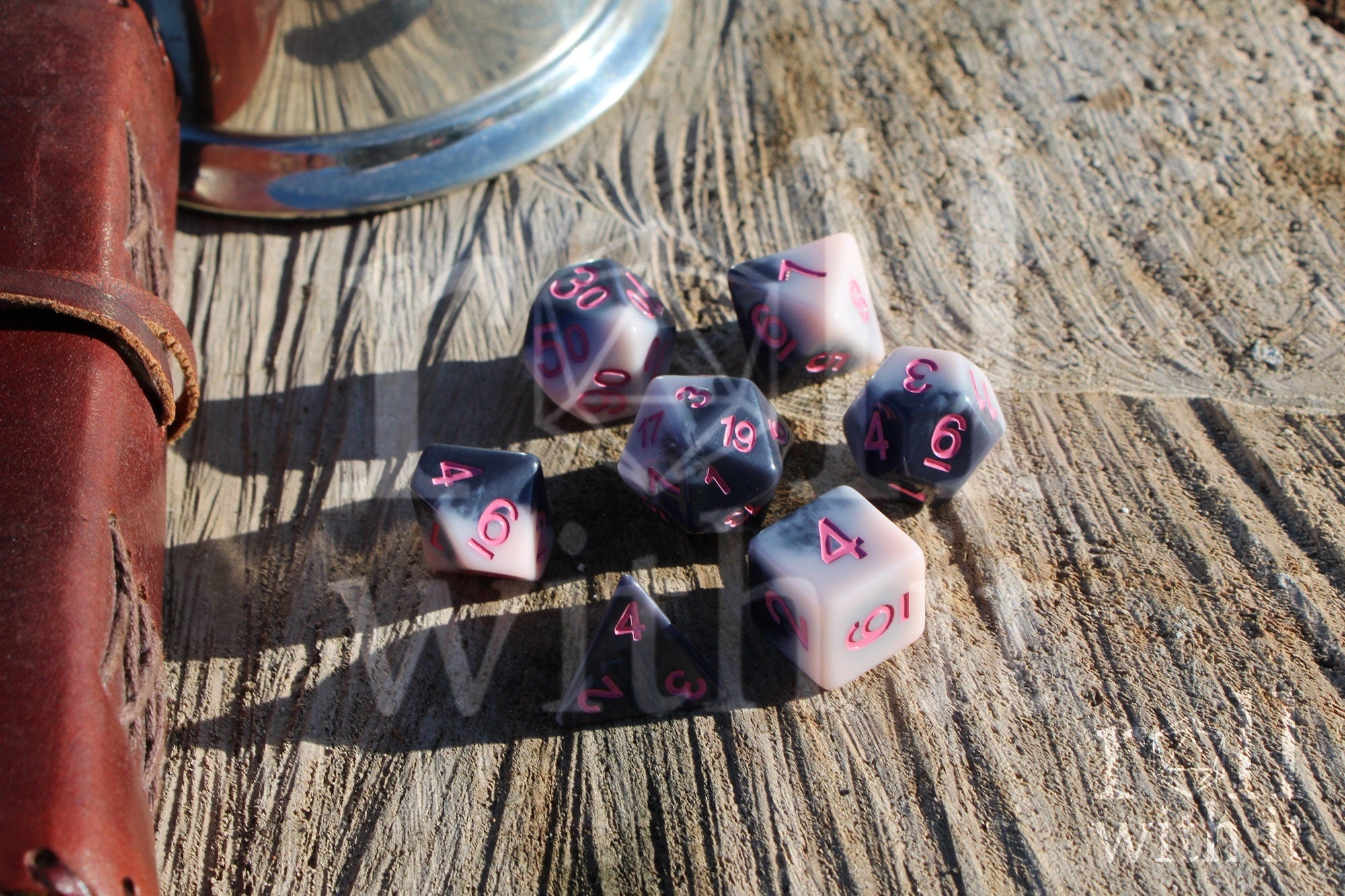 Set of pastel pink and grey polyhedral roleplaying dice with pink numbers sat on a wooden surface